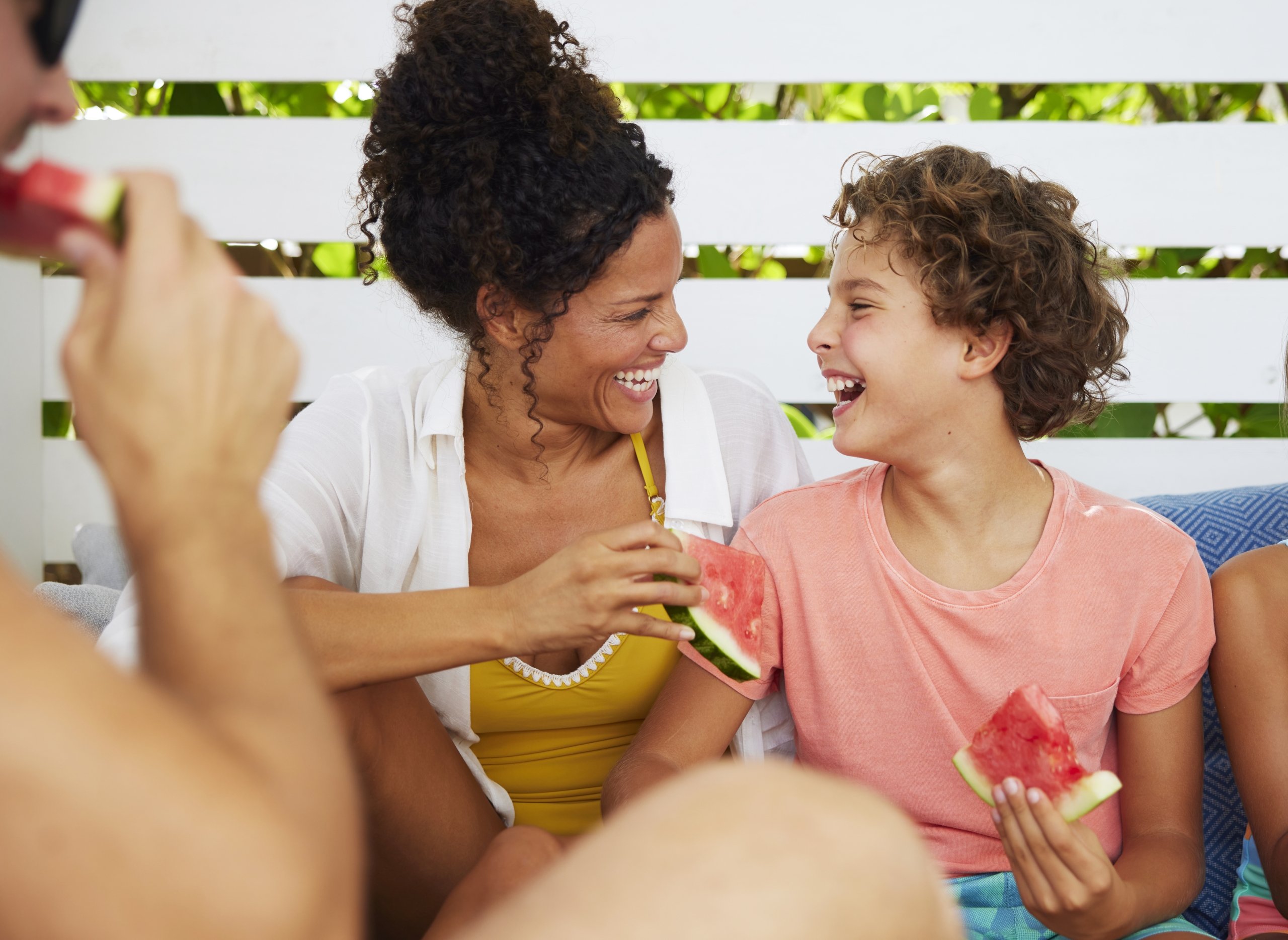 mom and son laughing and eating watermelon in a poolside cabana on vacation in florida