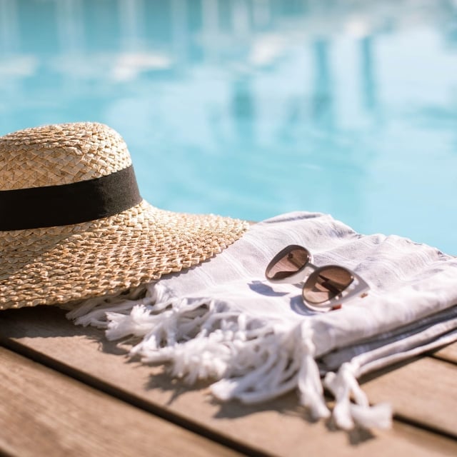 Sunglasses and straw hat on the wooden floor at the pool.