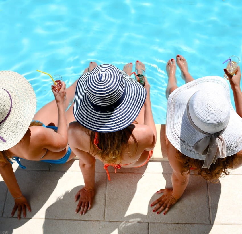 three beautiful young woman with sun hat sitting by the poolside